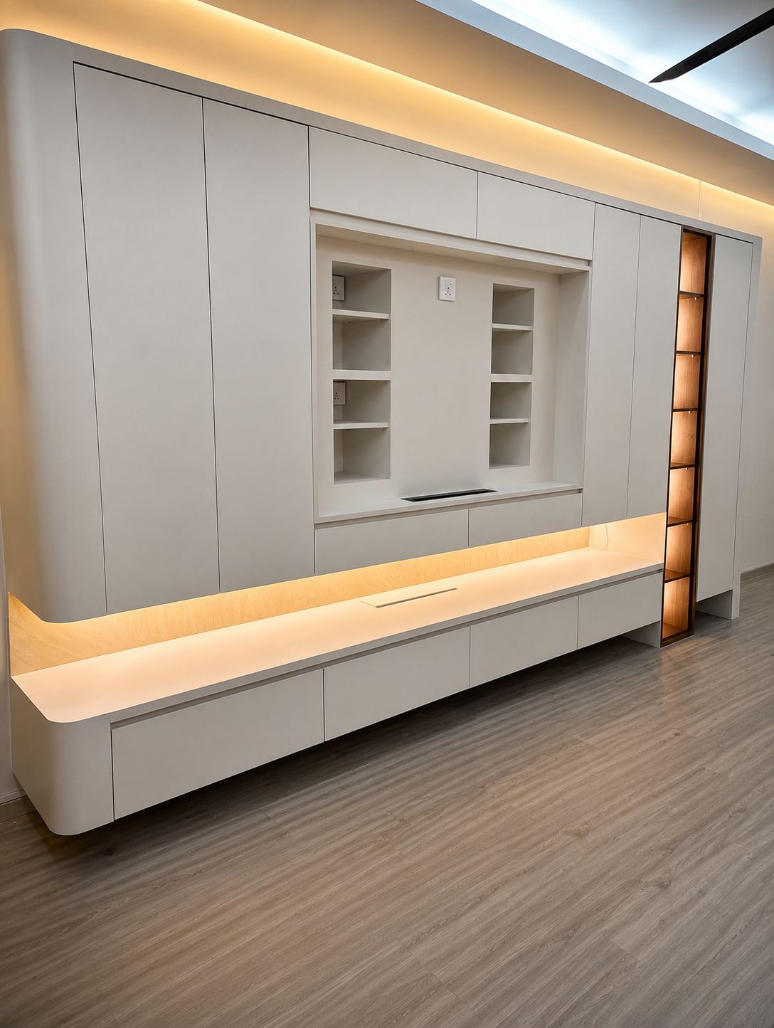 Angled view of the greige feature wall showing the floating cove-lit console and the glowing wood-lined LED display column
