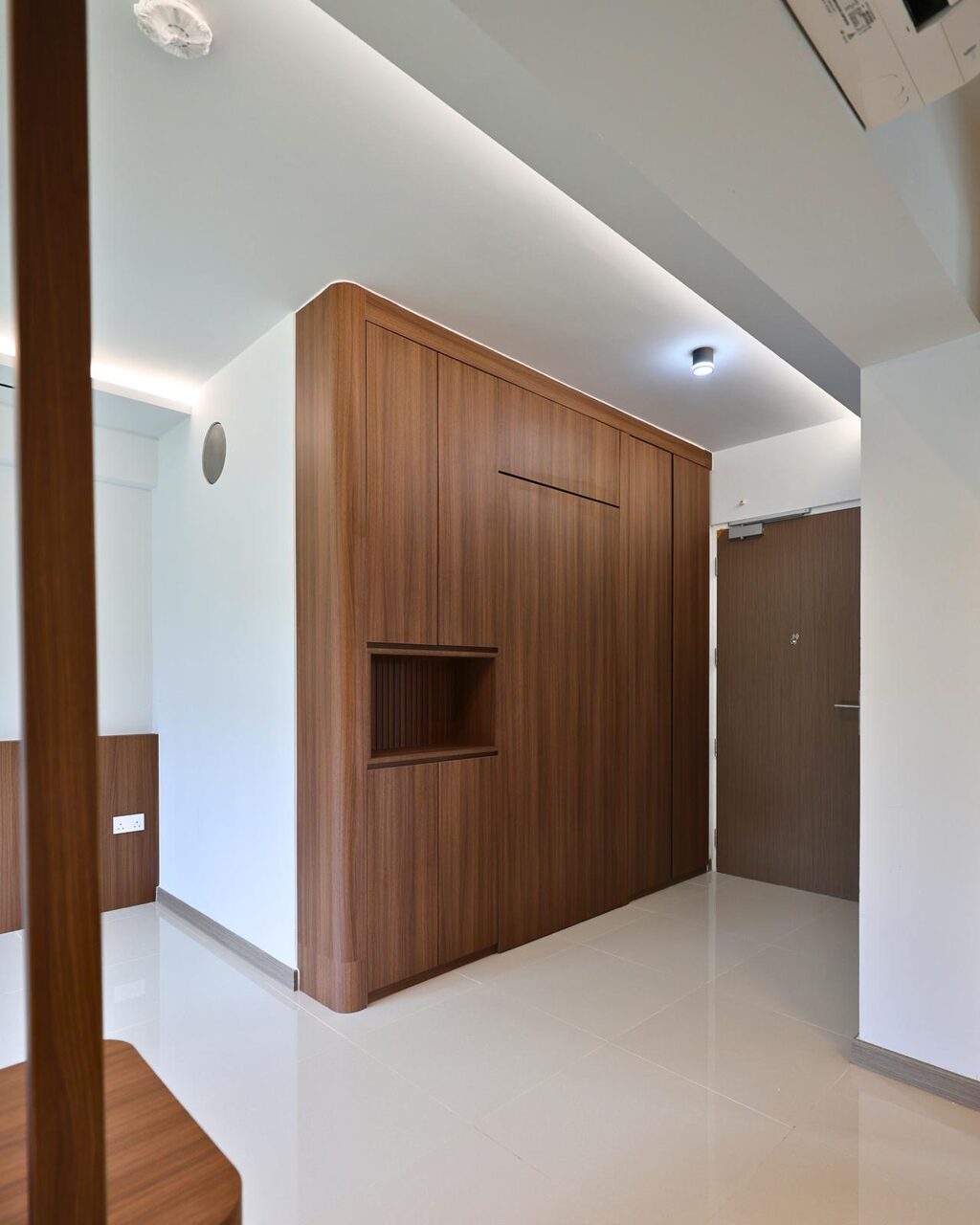 Full-height walnut entryway cabinet wrapping the corner with an open fluted niche and bench