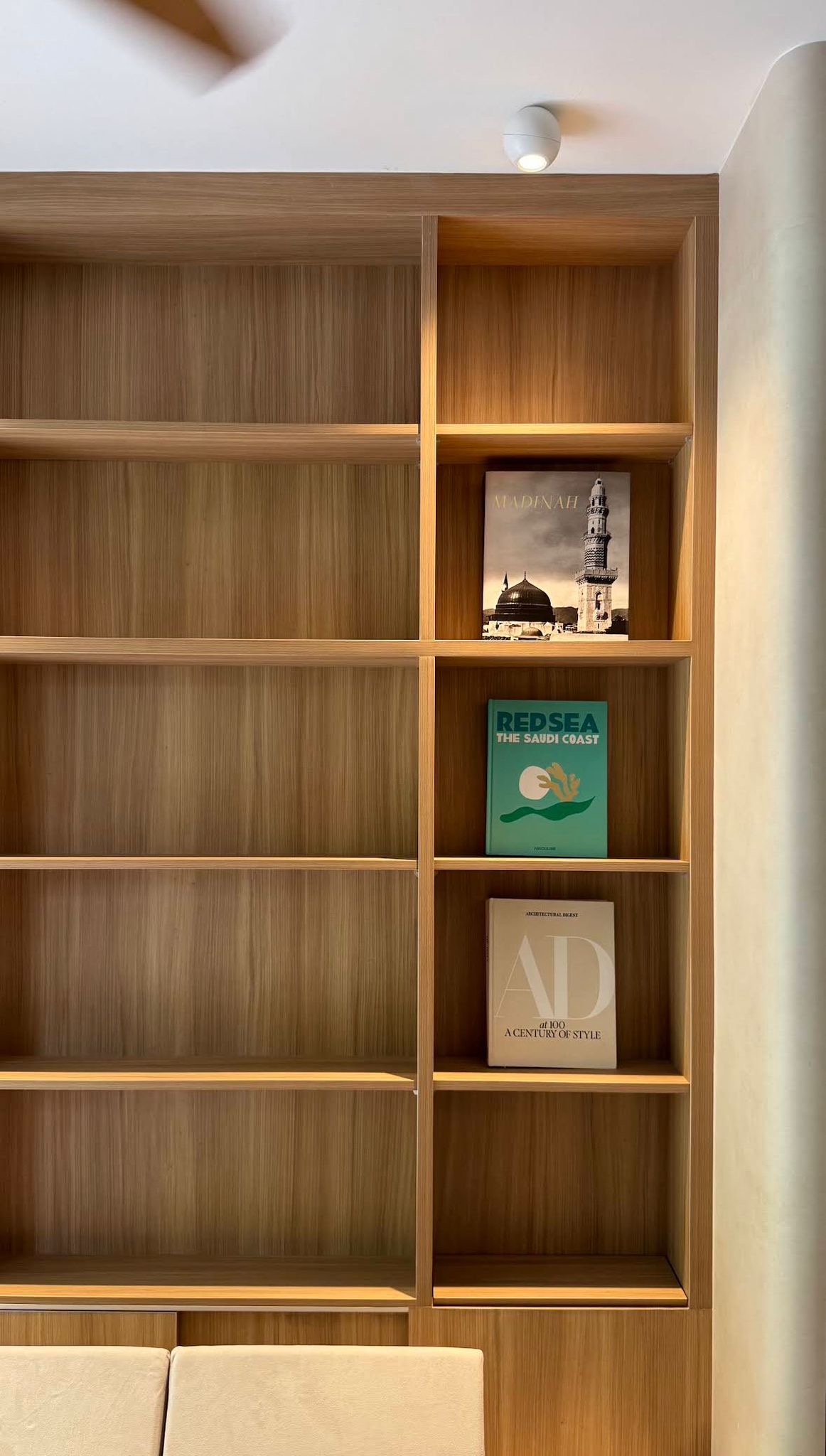 Detail of the oak open-grid shelving styled with coffee-table books beside the lime-plaster column